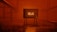 A retro television set displaying the word 'HELLO!' stands in a dimly lit, orange-hued environment. The room has an industrial feel with metal railings on either side, creating a symmetrical perspective leading to the TV.