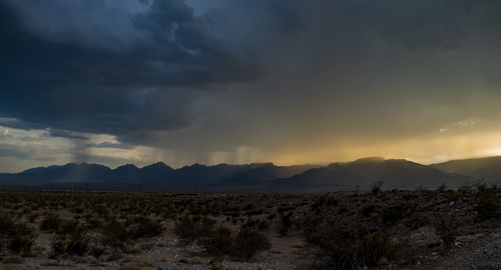 a storm rolls in over a desert with mountains in the background