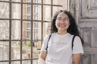 a woman wearing glasses standing in front of a wooden door