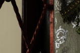 A detailed view of a decorative fabric with ornate silver patterns and fringes. A twisted rope is visible on the left side, set against a dark background.