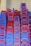 A large stack of plastic chairs arranged neatly against a wall. The chairs are predominantly blue and red, with each stack reaching considerable height, displaying a pattern created by alternating colors. The letters 'NTL' are visible on multiple chairs.