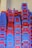 A large stack of plastic chairs arranged neatly against a wall. The chairs are predominantly blue and red, with each stack reaching considerable height, displaying a pattern created by alternating colors. The letters 'NTL' are visible on multiple chairs.
