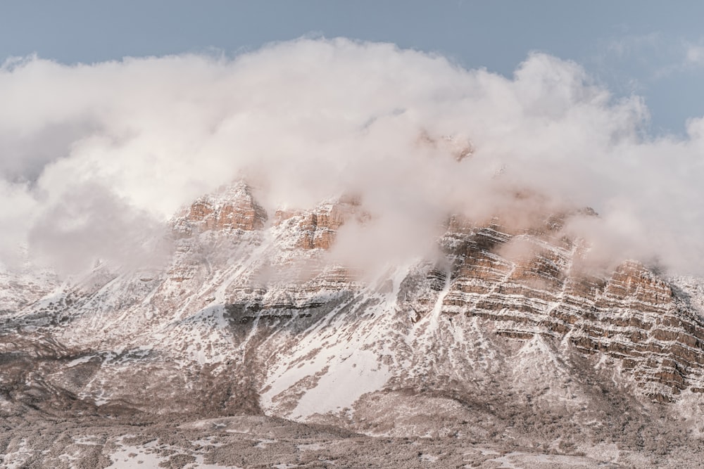 a mountain covered in snow and clouds under a blue sky