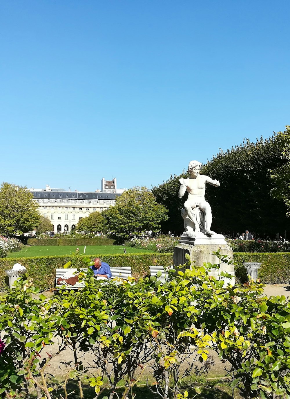 eine Statue eines Mannes, der auf einer Bank in einem Park sitzt