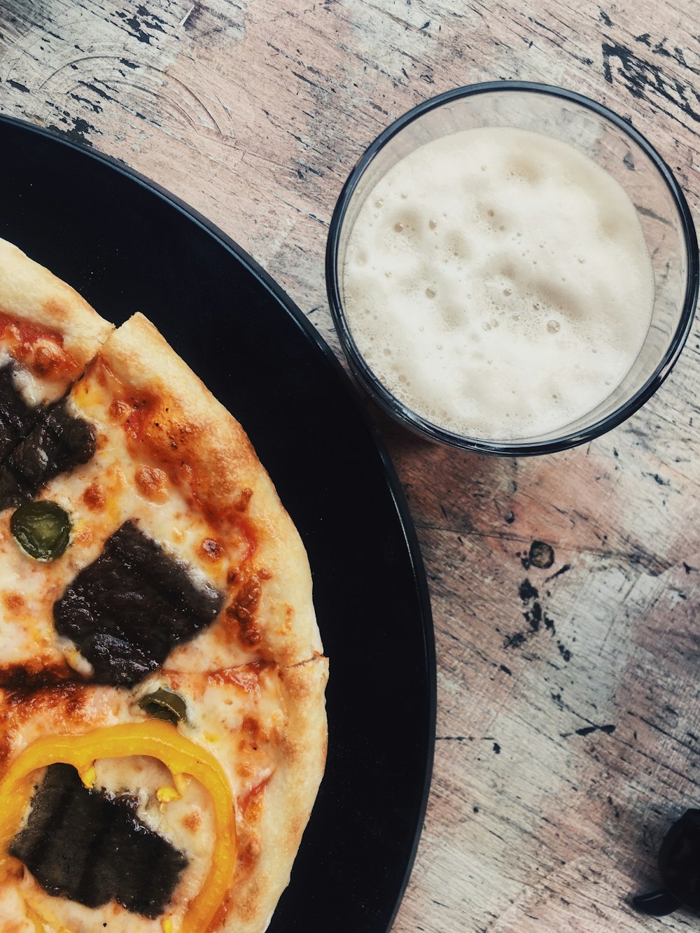 a pizza sitting on top of a black plate next to a glass of beer