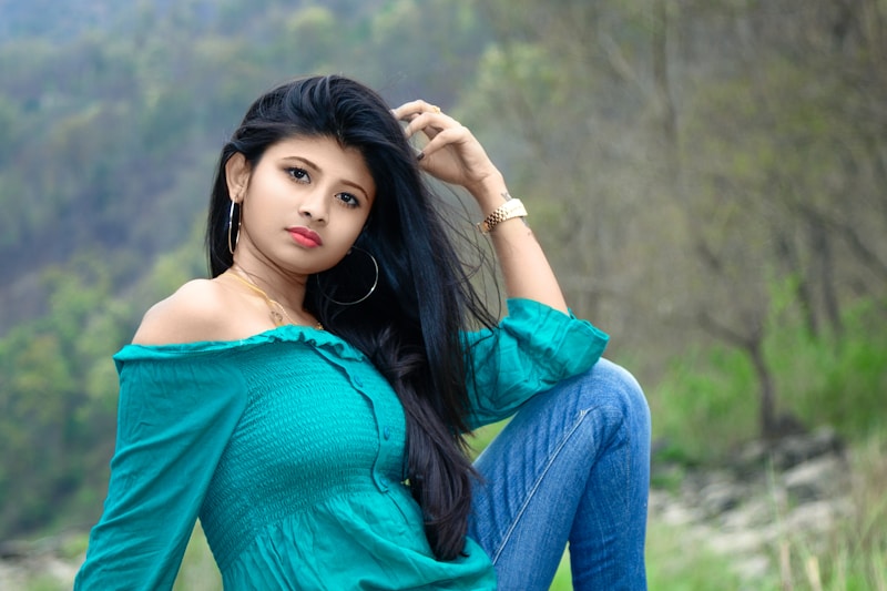 a woman with long black hair sitting in a field