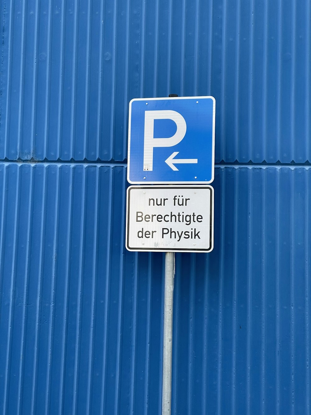 a parking sign on a pole in front of a blue wall