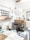 A creative studio space featuring a letterpress and linoprint workshop with printed artworks and tools. Posters with inspirational messages are suspended from the ceiling. A well-organized, artistic workspace with a wooden type cabinet and various paper materials. The room is bright and airy, with a window providing natural light.