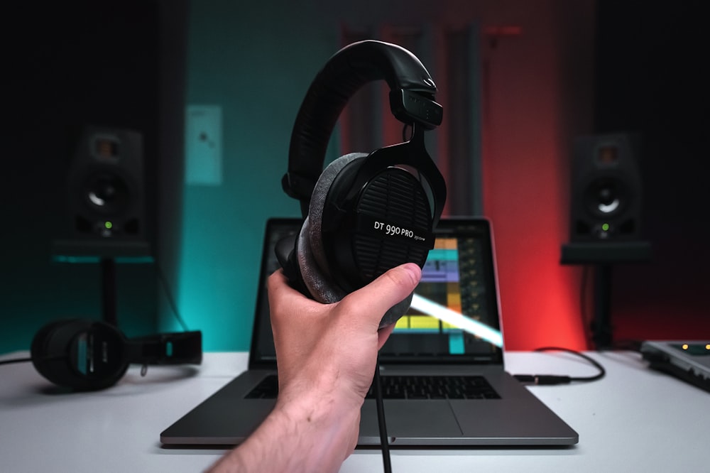 a person holding a pair of headphones in front of a laptop