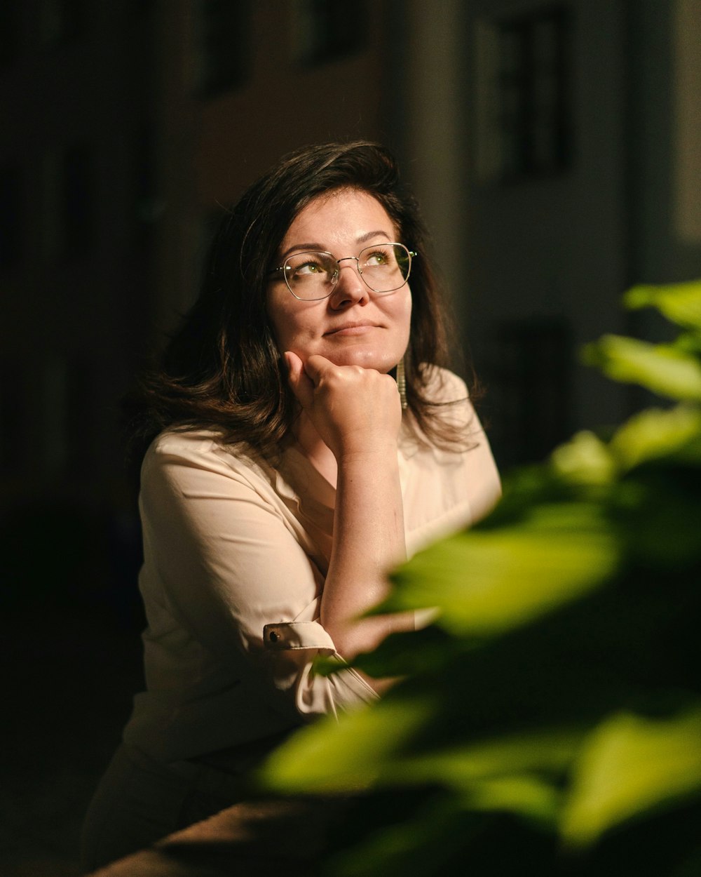 a woman with glasses sitting in front of a plant