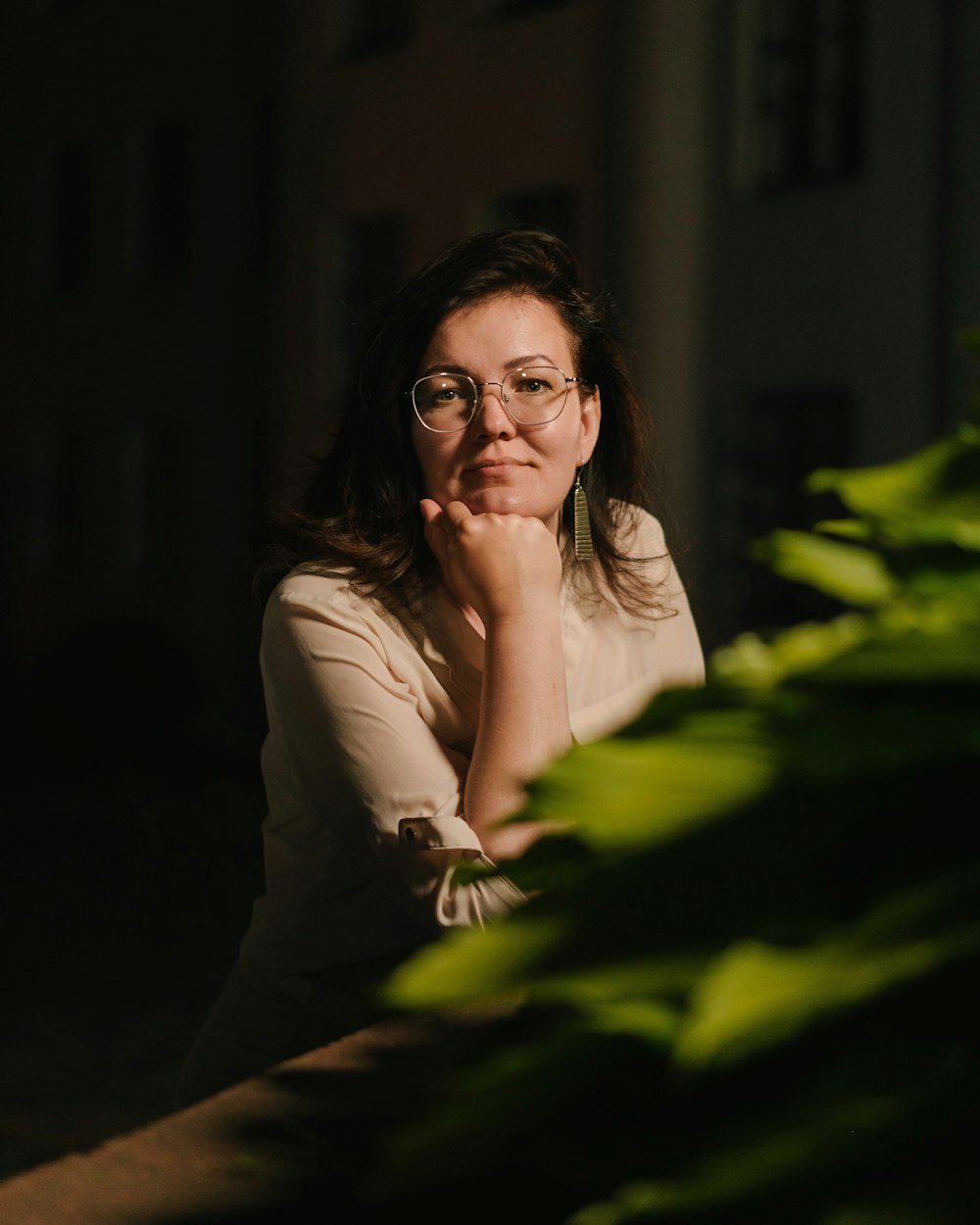 a woman wearing glasses sitting in front of a plant