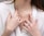 A close-up of a woman's torso showcasing delicate jewelry, including multiple gold necklaces with pendants, and several gold and gemstone rings on her fingers. She is wearing a white blouse, adding contrast to the jewelry.
