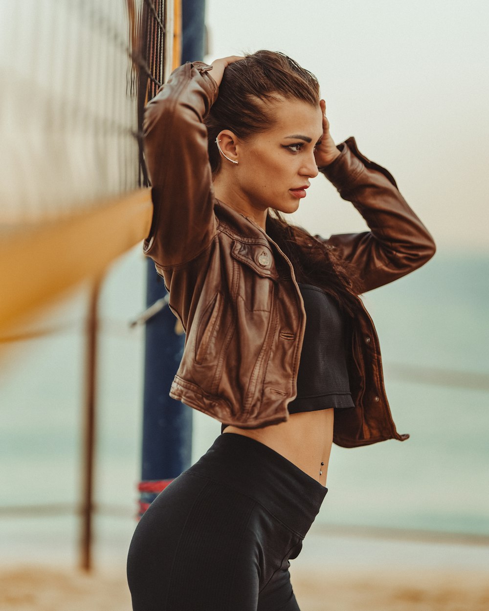 a woman in a leather jacket leaning against a volleyball net