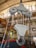 A large industrial hook attached to a pulley system is prominently displayed in a warehouse setting. The surroundings feature multiple chains and industrial equipment with a high ceiling and bright lighting.