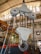 A large industrial hook attached to a pulley system is prominently displayed in a warehouse setting. The surroundings feature multiple chains and industrial equipment with a high ceiling and bright lighting.