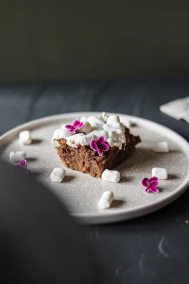 A pastel-colored ice cream cake adorned with delicate floral decorations, set on a simple white plate with soft natural lighting.