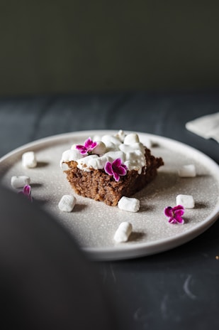 An elegant slice of homemade cake on a beige ceramic plate, surrounded by delicate dried flowers.