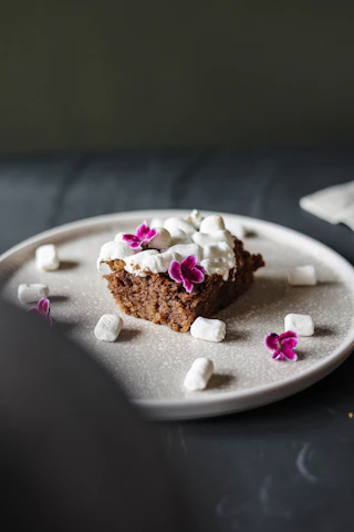 A close-up of a beautifully decorated artisanal cake on a minimalist cream-colored plate, bathed in soft natural light.