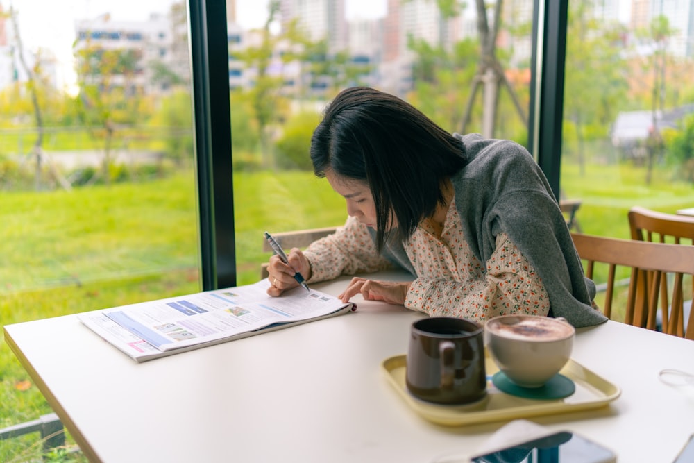 a woman sitting at a table writing on a piece of paper