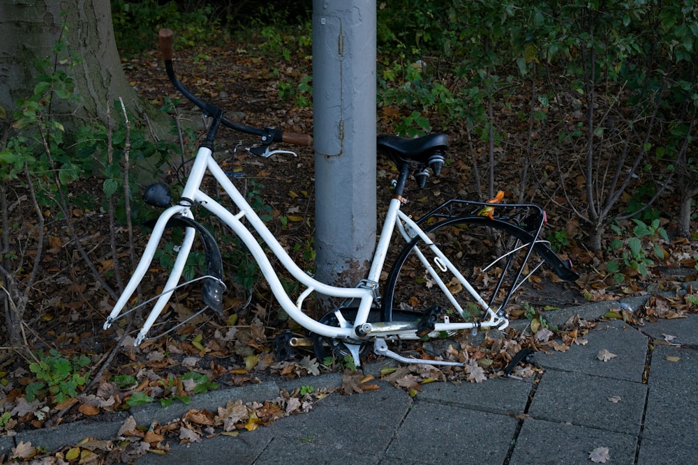 a white bicycle leaning against a pole on a sidewalk