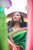 A graceful woman draped in a deep peacock green saree with golden embroidery, standing against a warm cream backdrop.