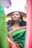 A graceful woman draped in a deep emerald green neelambara saree, standing against a softly lit traditional backdrop.