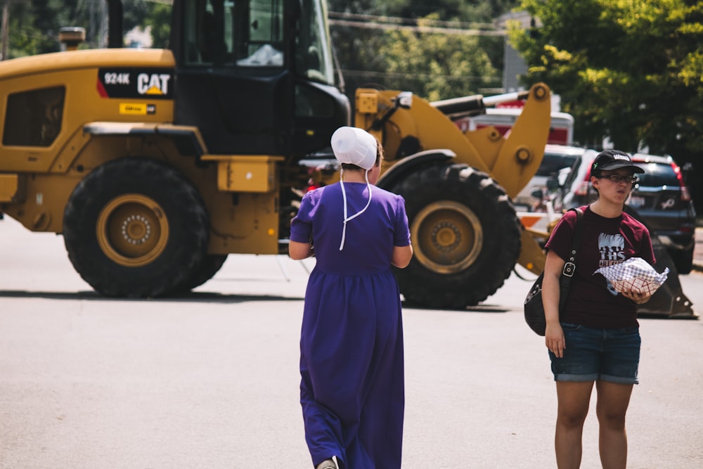 a woman in a purple dress is standing in front of a bulldozer