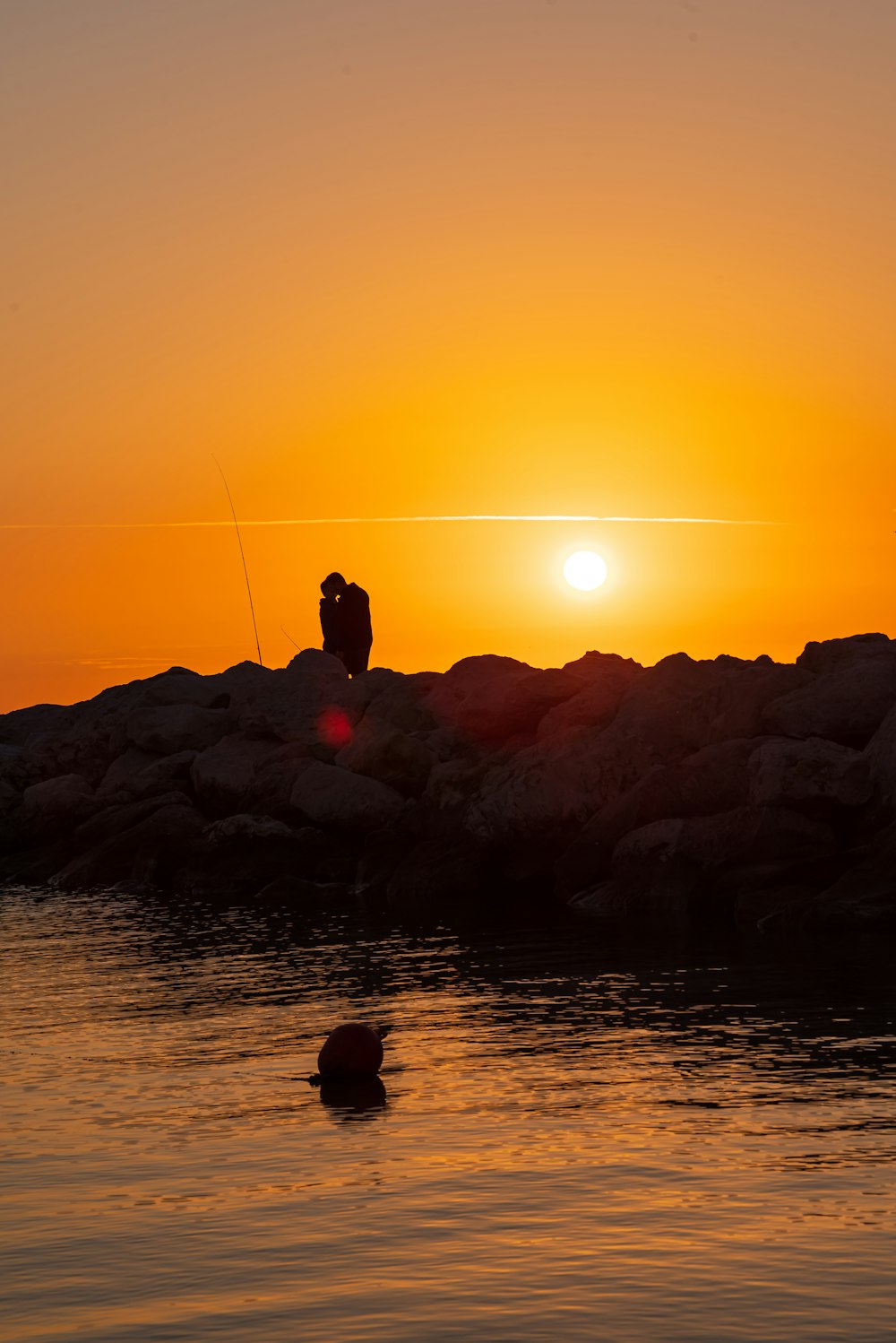 um homem pescando na água ao pôr do sol