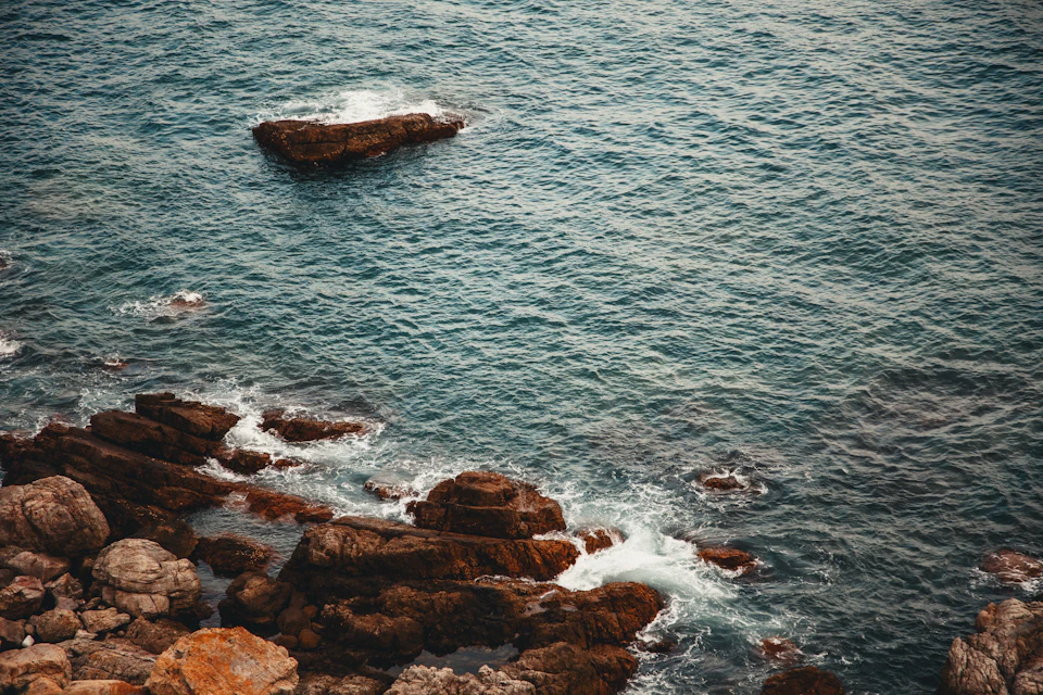 Serene coastal scene with rocky shoreline, deep blue ocean, and overcast sky above