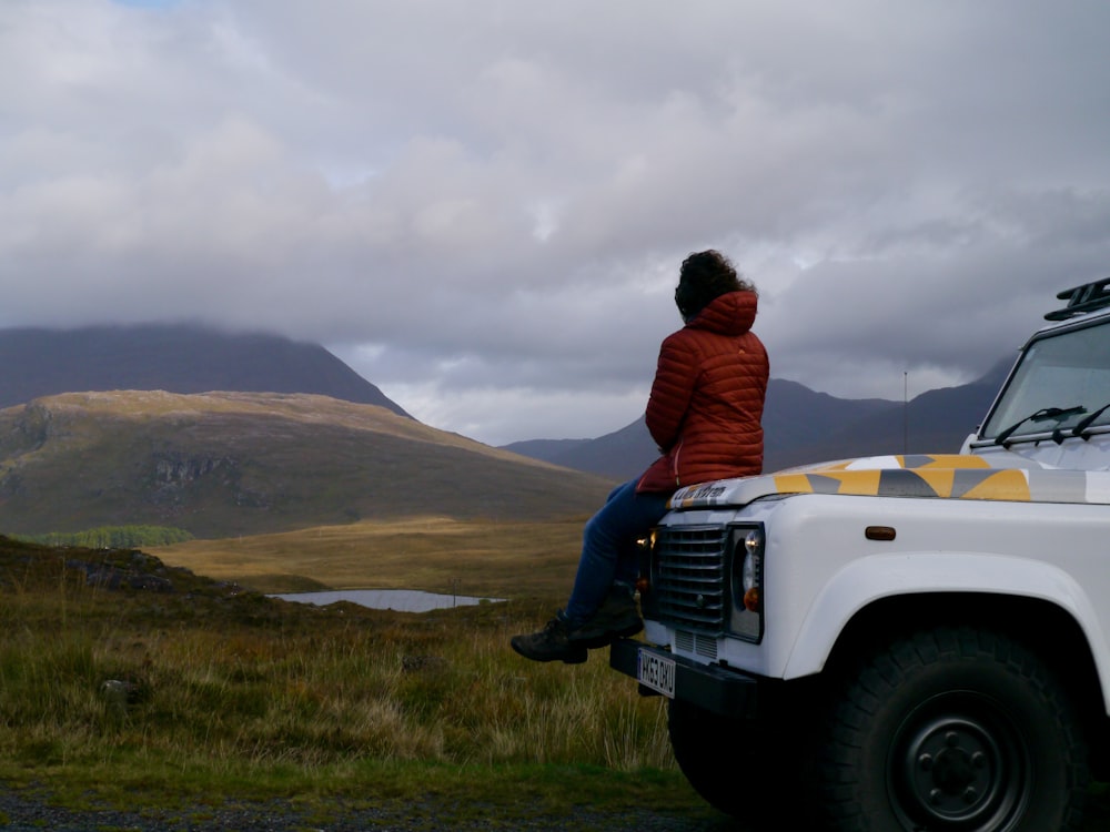 a man in a red jacket sitting on the hood of a white truck