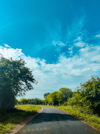 A scenic view of a winding road surrounded by lush greenery and blue skies.