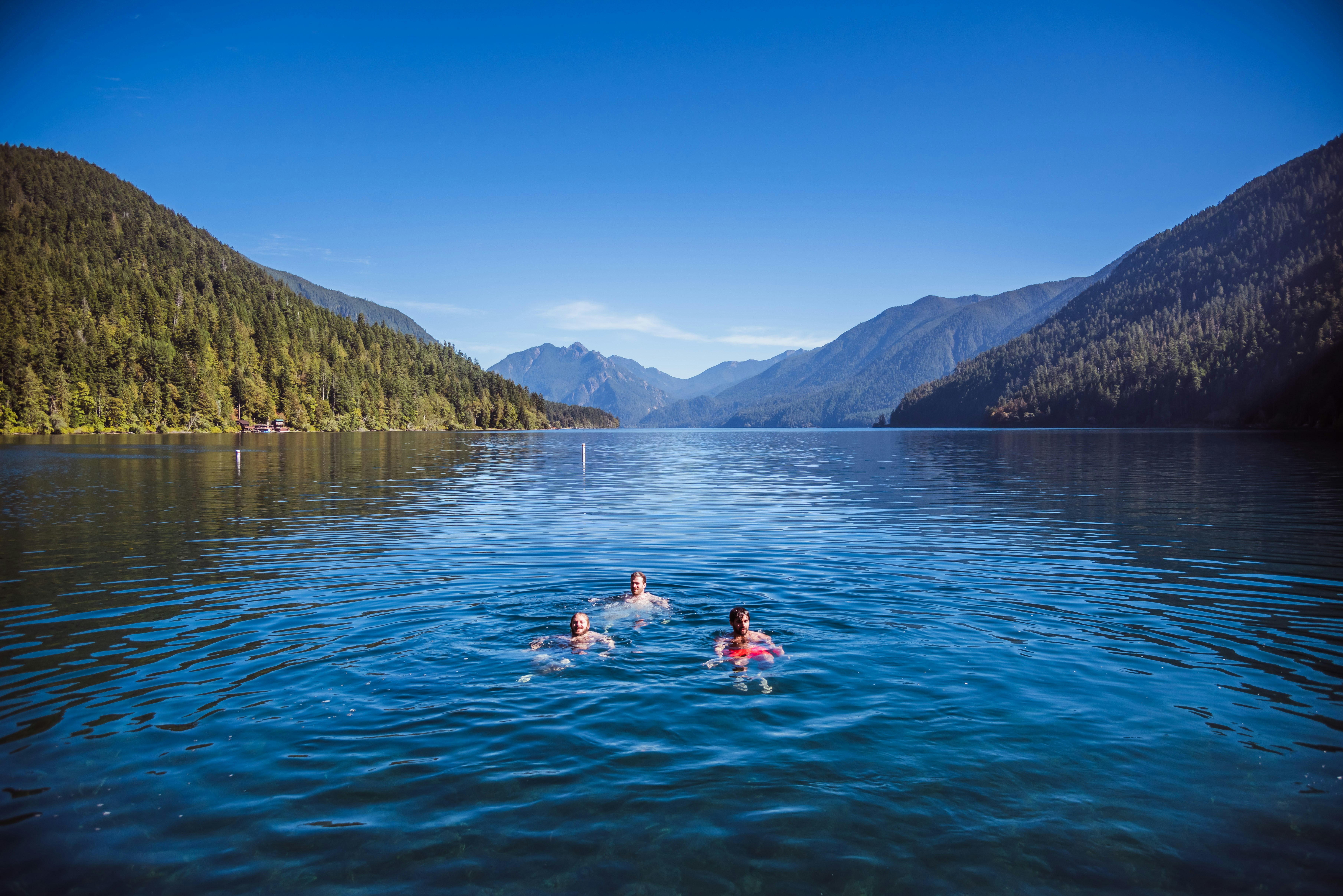 two people swimming in a lake surrounded by mountains