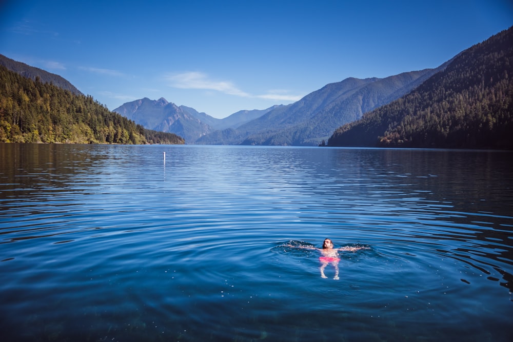 a person swimming in a lake with mountains in the background