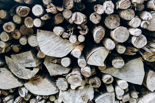 A tightly packed stack of cut tree logs, featuring various sizes and shapes. The texture of the wood grain and the natural patterns on the cut surfaces are clearly visible.