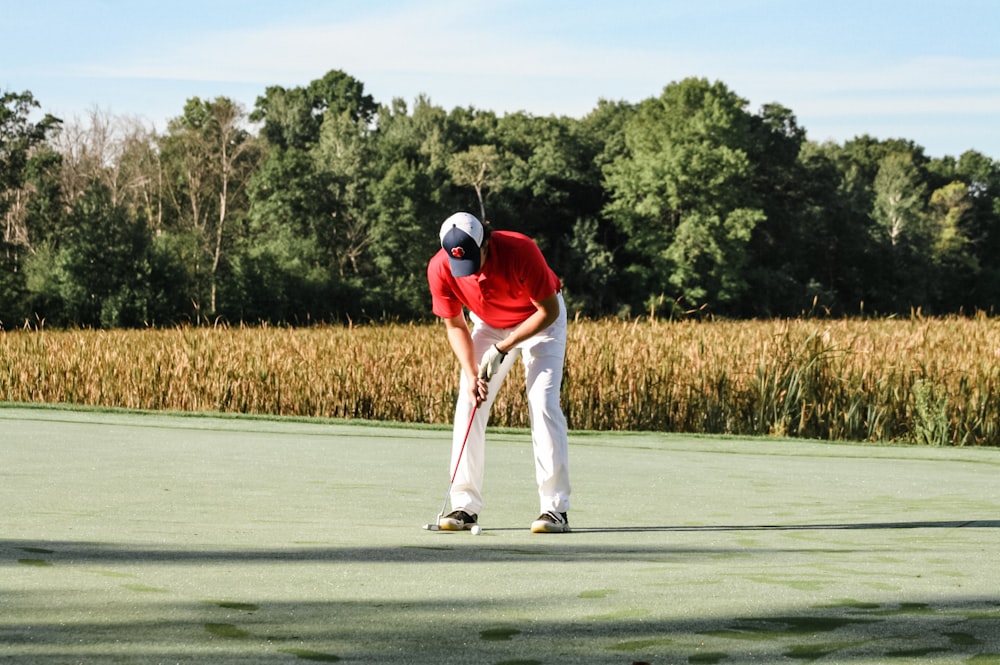 a man in a red shirt and white pants playing a game of golf