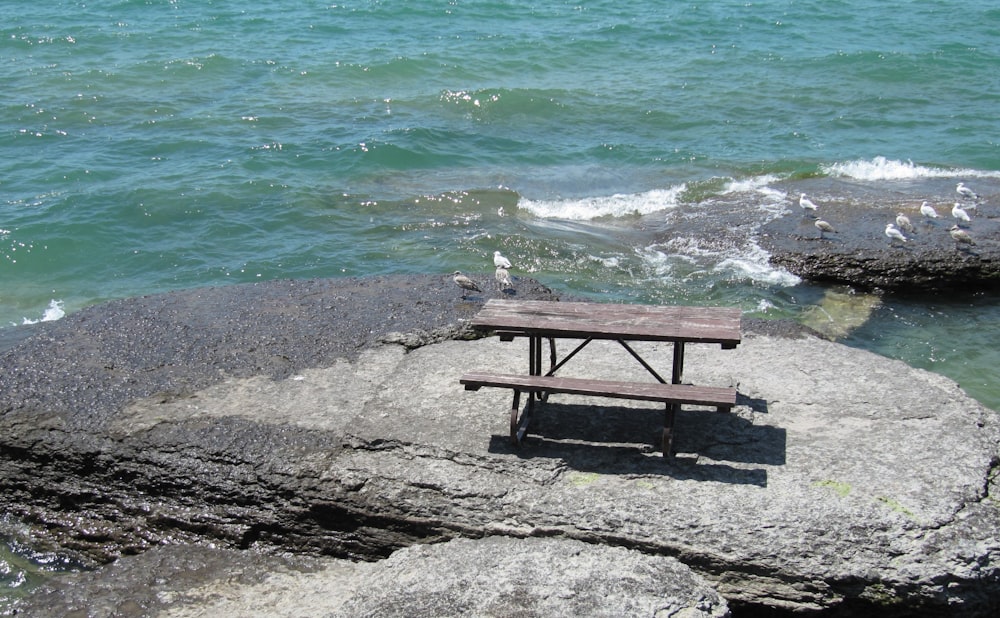 a picnic table sitting on top of a rock next to the ocean