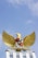 A golden eagle with its wings spread wide stands atop a white structure. Its chest is adorned with a shield containing various symbols. Below the eagle is an inscribed banner. The sky is clear and blue, providing a serene backdrop.