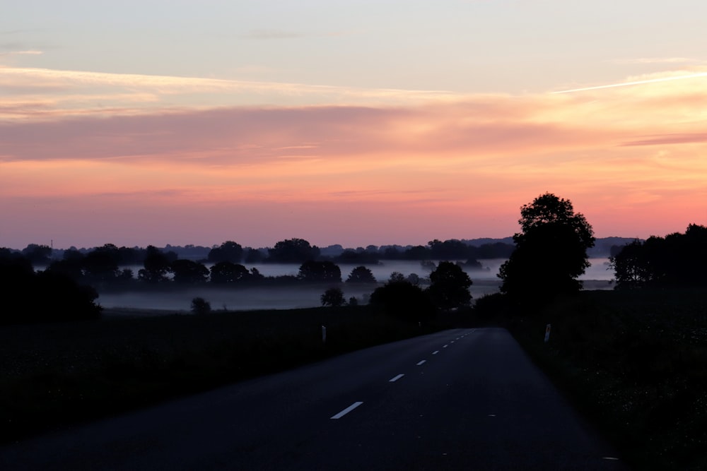 the sun is setting over a rural road