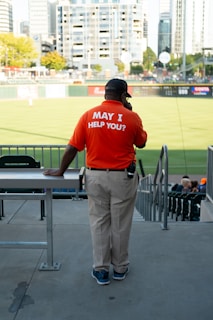 a man in an orange shirt stands at a baseball field