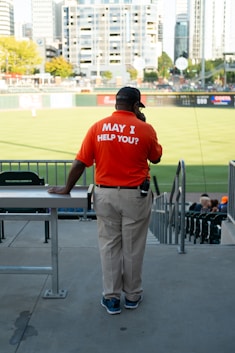 a man in an orange shirt stands at a baseball field