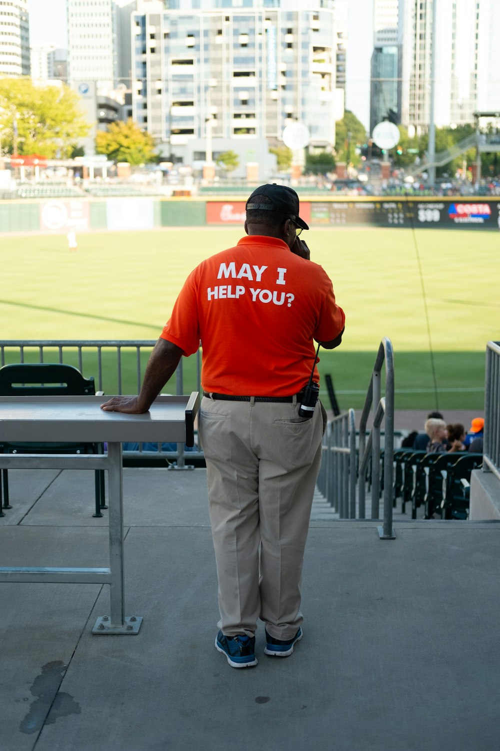 a man in an orange shirt stands at a baseball field