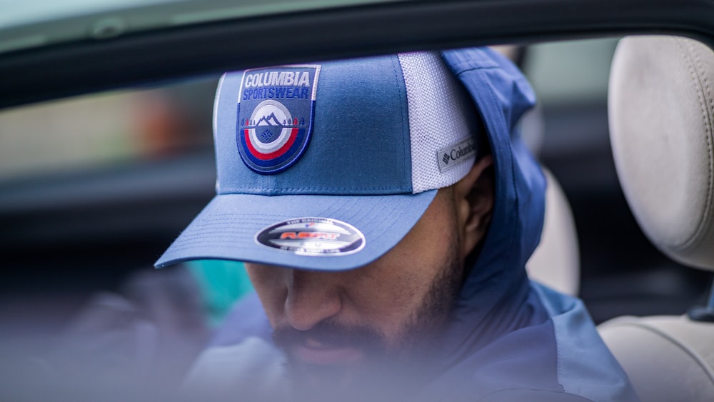 a man sitting in a car wearing a blue hat