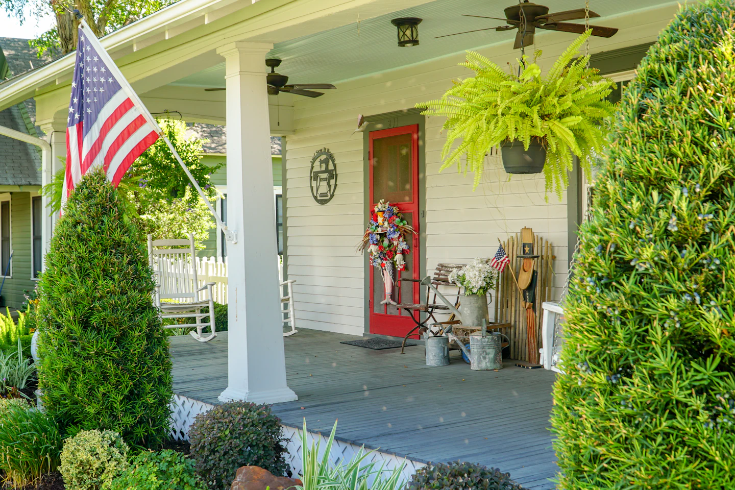 Classic front porch with hanging ferns, a flag and a red door