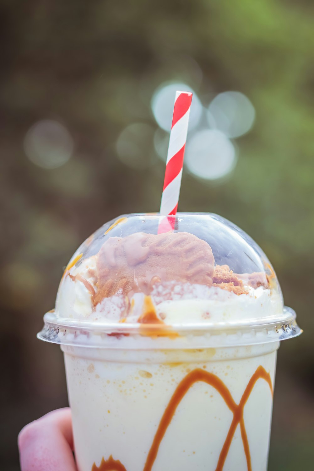 a hand holding a cup of ice cream with a straw