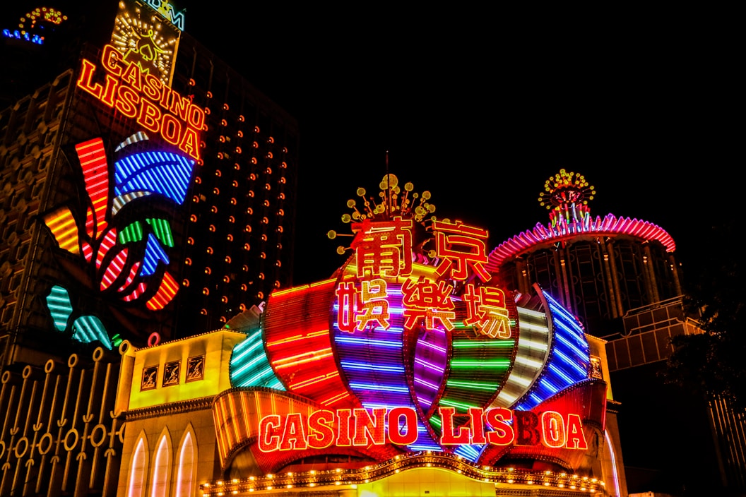 Bright neon lights and colorful signage adorn the exterior of Casino Lisboa, creating a vibrant and lively atmosphere. The façade features bold, multicolored designs with a mix of English and Chinese characters prominently displayed. The lights form intricate patterns and shapes, contributing to the energetic ambiance of the scene.