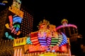 Bright neon lights and colorful signage adorn the exterior of Casino Lisboa, creating a vibrant and lively atmosphere. The façade features bold, multicolored designs with a mix of English and Chinese characters prominently displayed. The lights form intricate patterns and shapes, contributing to the energetic ambiance of the scene.