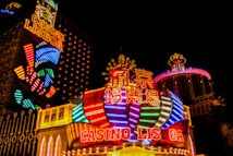 Bright neon lights and colorful signage adorn the exterior of Casino Lisboa, creating a vibrant and lively atmosphere. The façade features bold, multicolored designs with a mix of English and Chinese characters prominently displayed. The lights form intricate patterns and shapes, contributing to the energetic ambiance of the scene.
