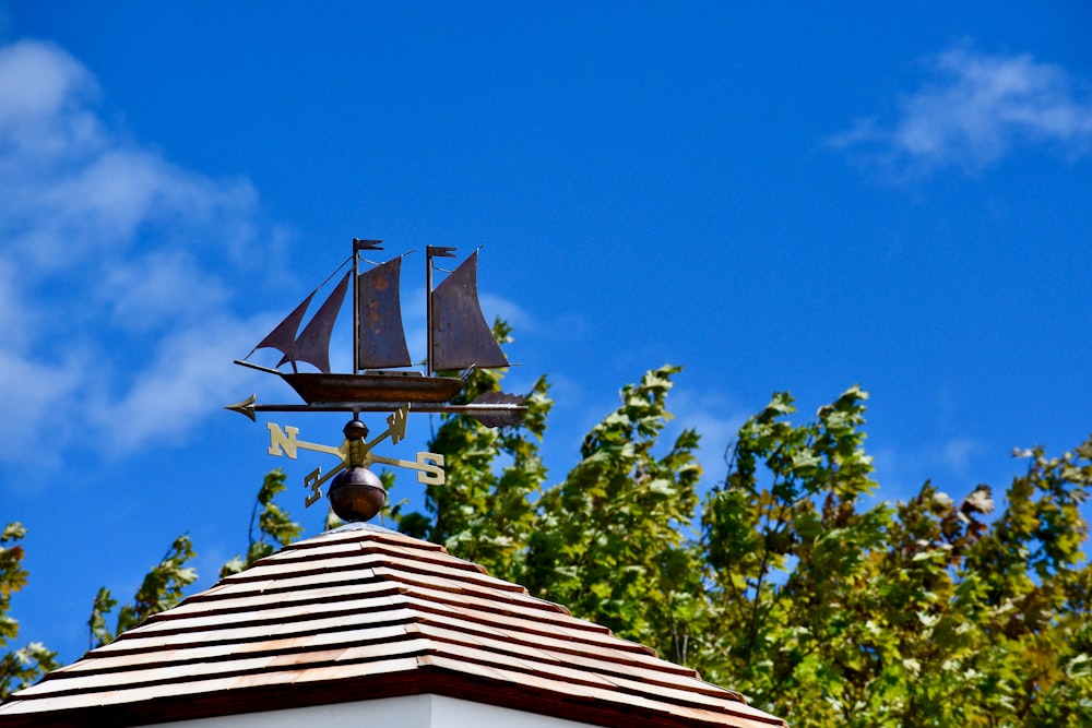 a weather vane on top of a roof with a sailboat on it