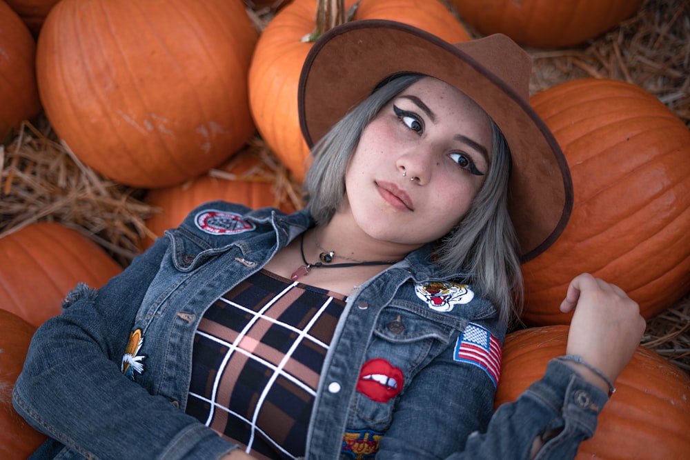 a woman in a cowboy hat laying on a pile of pumpkins