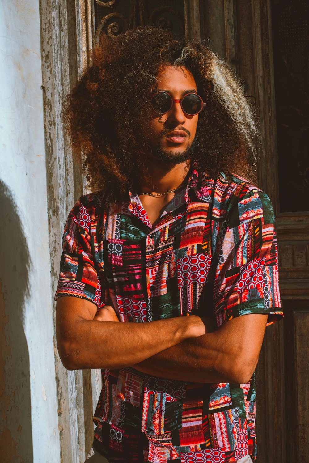 a man with long hair and sunglasses standing with his arms crossed